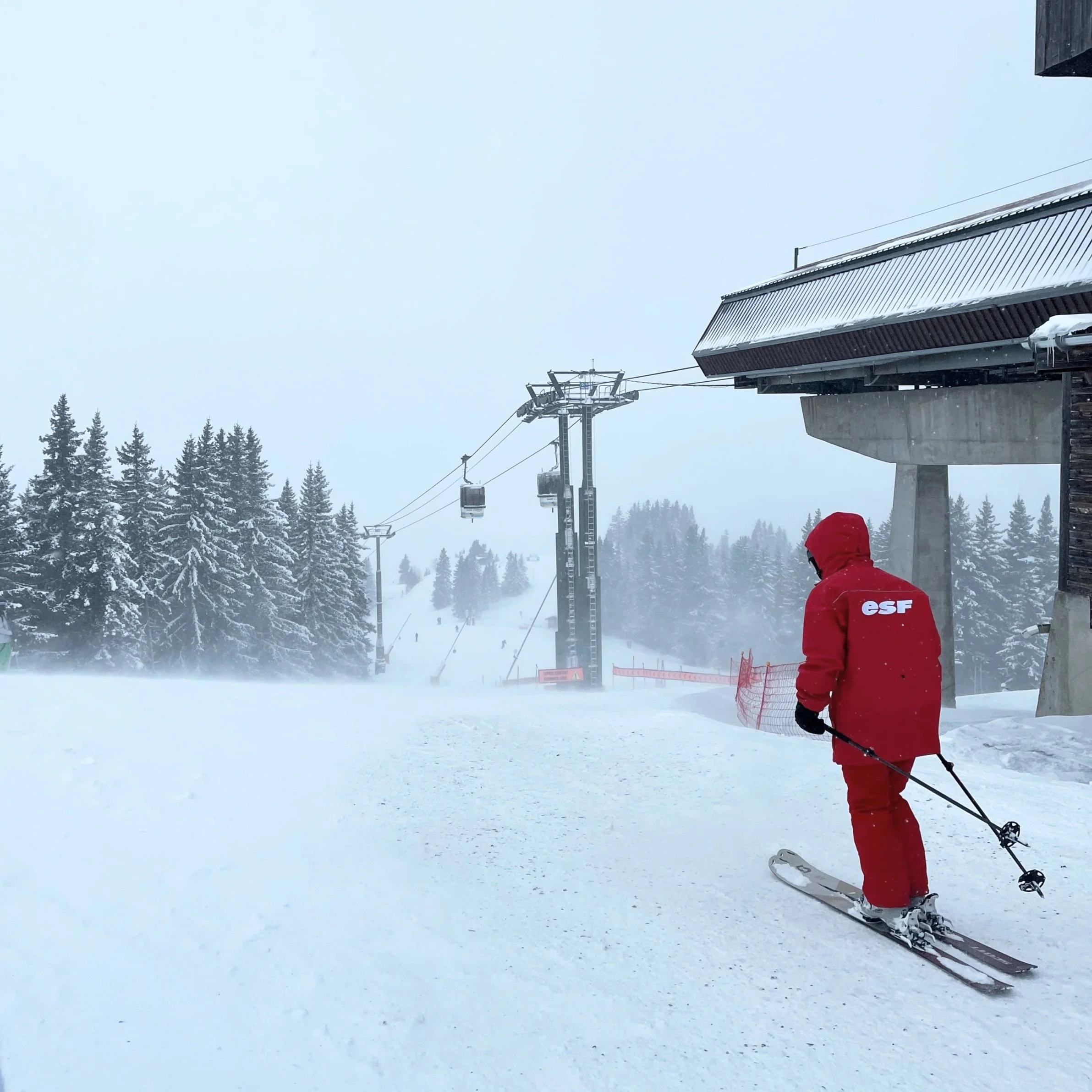 A skier contemplates a piste at the top of the mountain in reduced visibility.