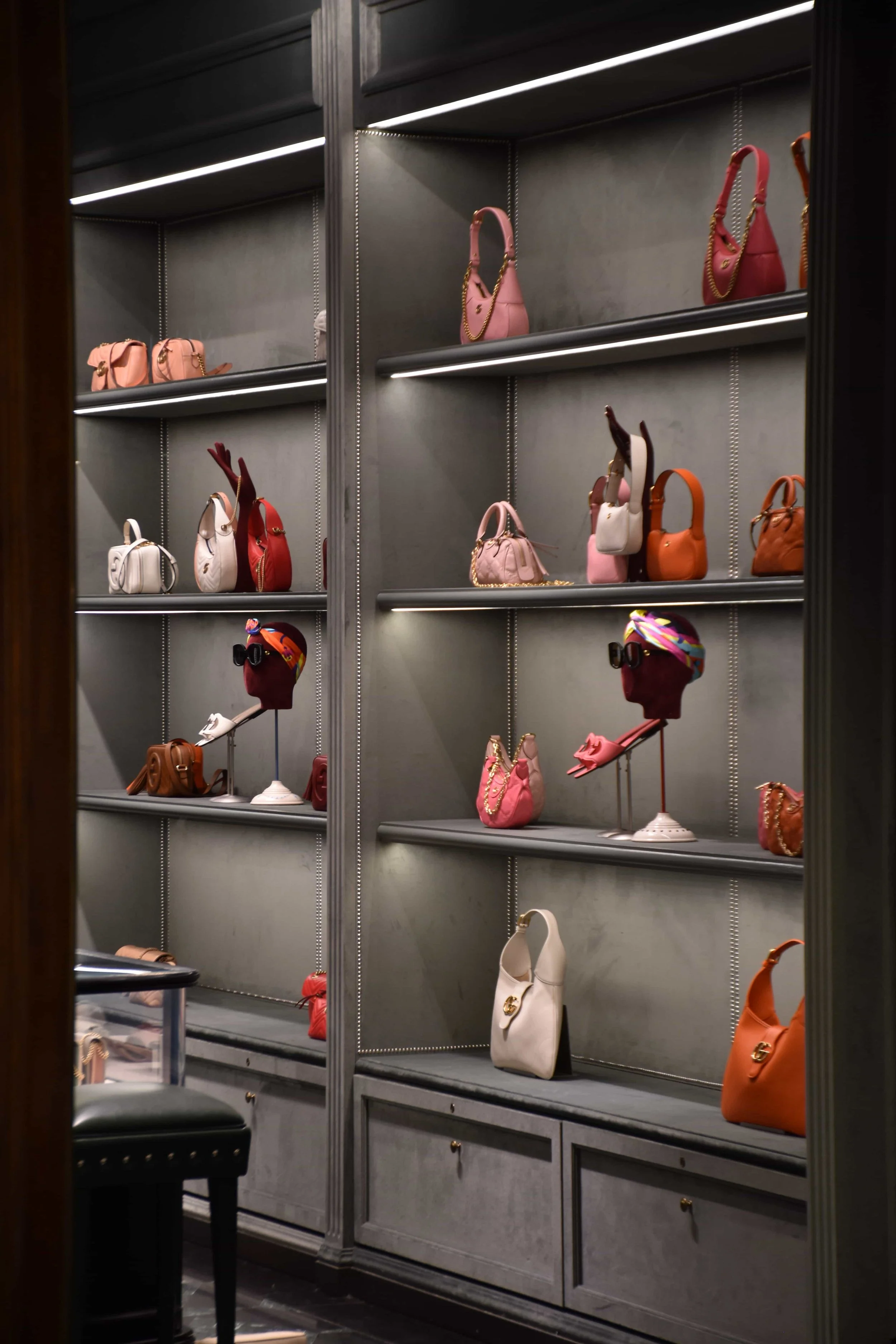 An interior shelf in a Gucci boutique, filled with handbags and scarfs in pinks and reds.