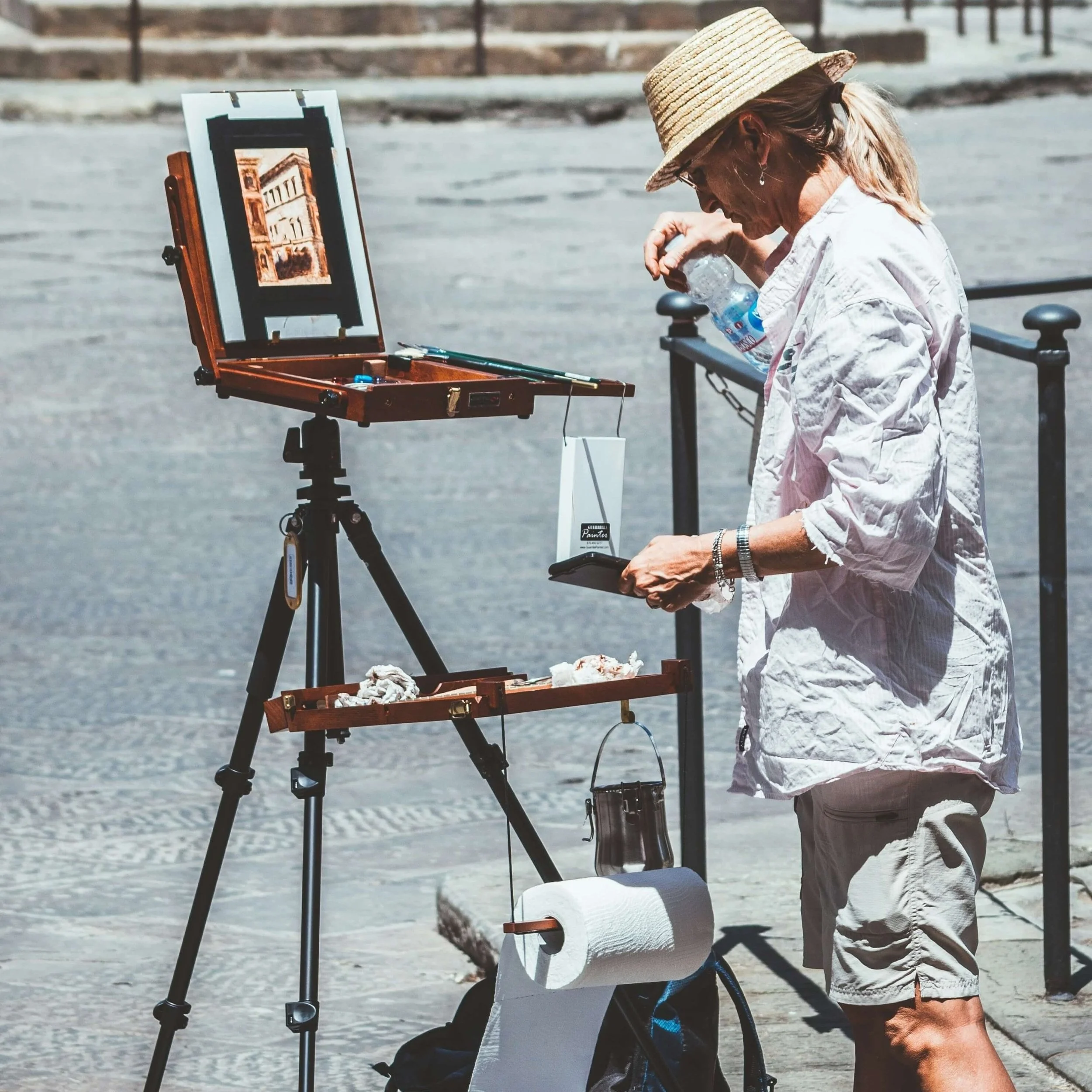 A painter stands at a portable easle while painting outdoors.
