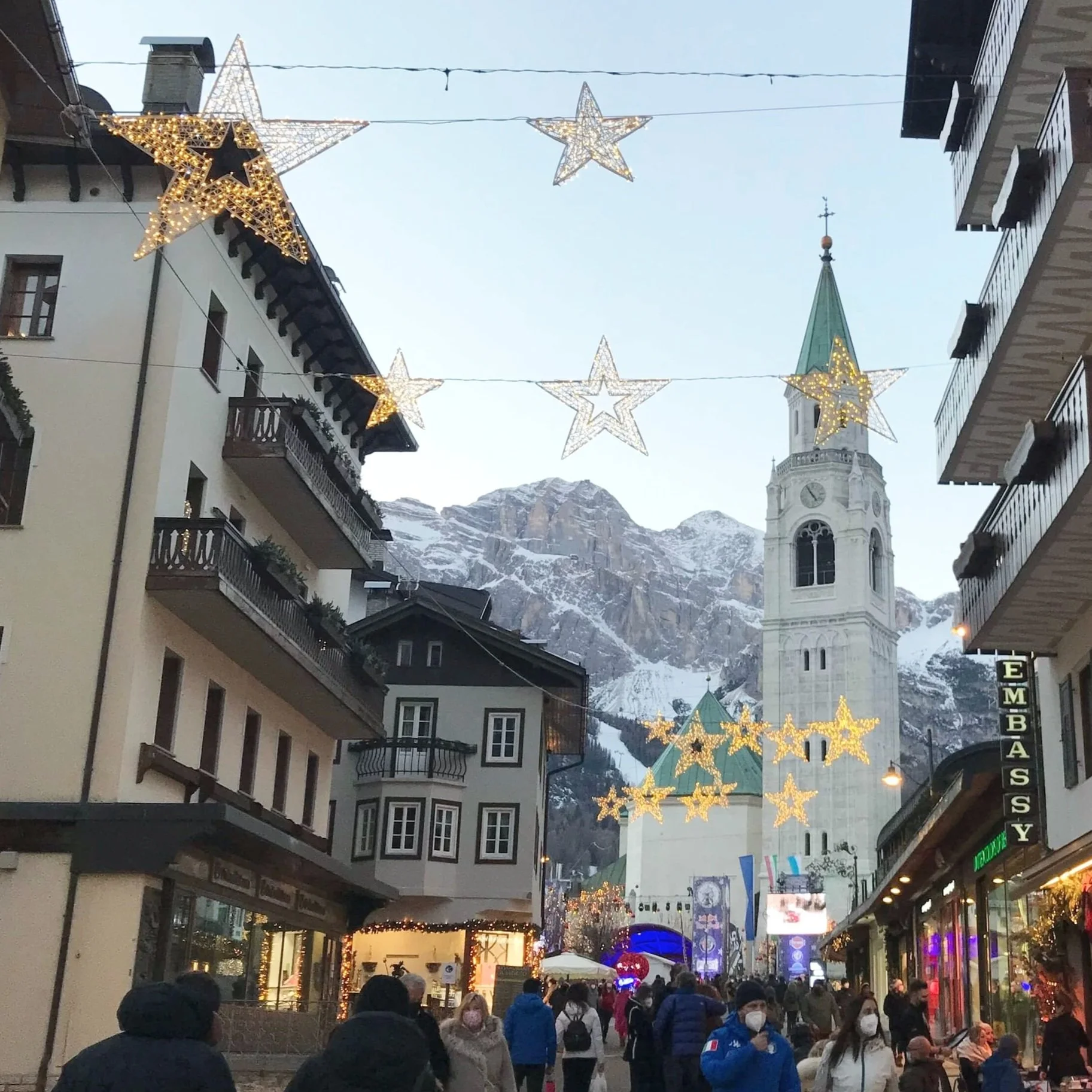 View of the bell tower of Cortina d'Ampezzo with twinkling star lights in front of it.